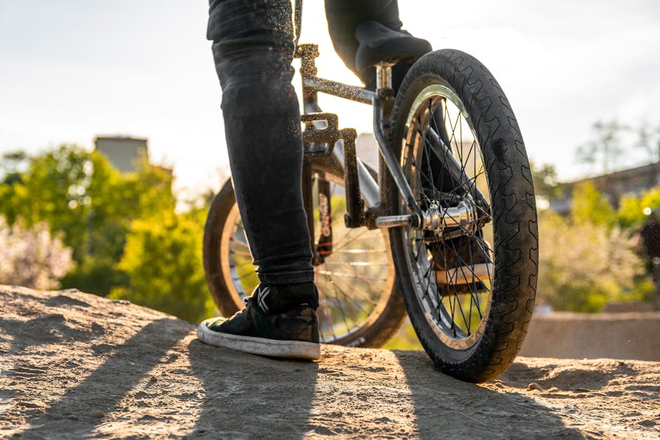 Close-up of a BMX biker standing on dirt in a bright outdoor setting.