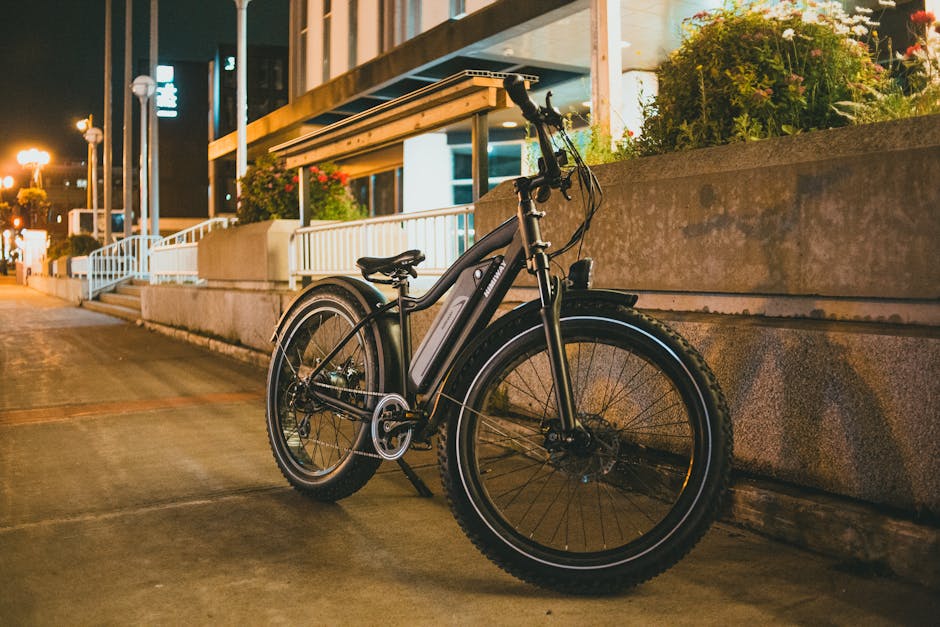 A bicycle is parked on a city street at night, surrounded by modern architecture and plants.