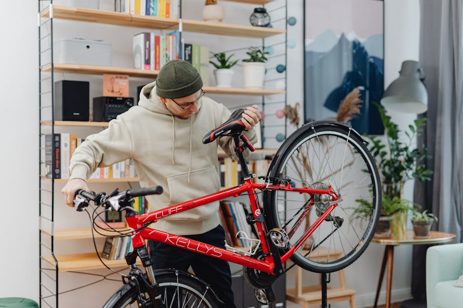 A man in a hoodie repairs a red bicycle in a cozy indoor setting with shelves and plants.